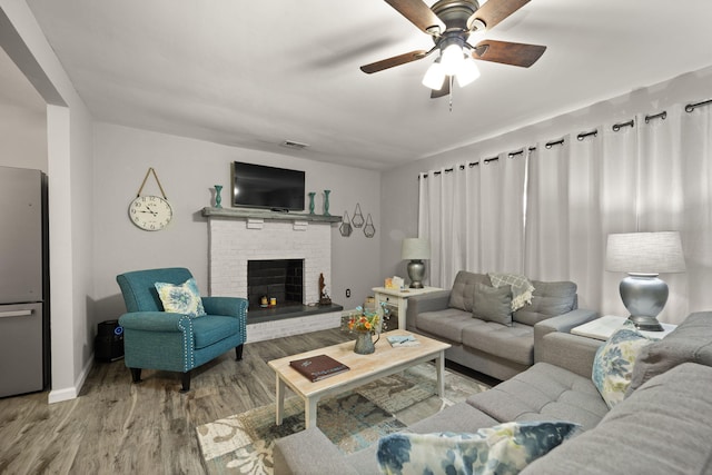 living room with ceiling fan, wood-type flooring, and a brick fireplace