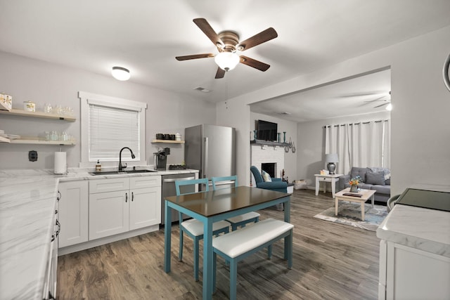 kitchen with dark wood-type flooring, sink, white cabinetry, a brick fireplace, and stainless steel appliances