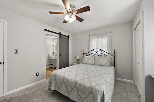 bedroom with ensuite bathroom, light colored carpet, ceiling fan, a barn door, and a closet