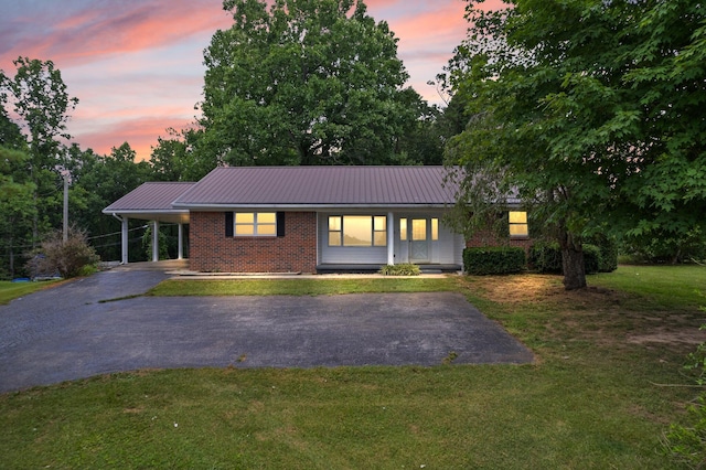 ranch-style house with brick siding, metal roof, aphalt driveway, an attached carport, and a front yard