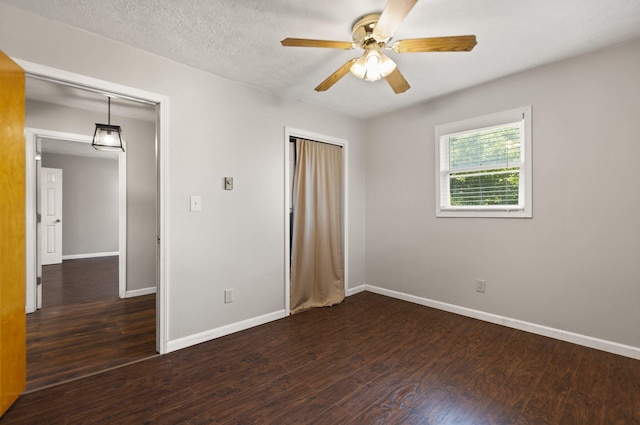 unfurnished bedroom with a textured ceiling, ceiling fan, dark wood-type flooring, and baseboards