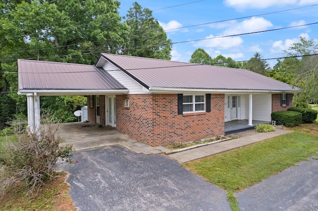 ranch-style house with metal roof, aphalt driveway, a porch, a carport, and brick siding