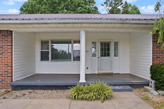 view of exterior entry with metal roof, brick siding, and a porch