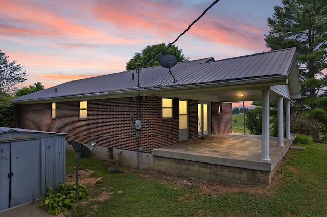 back of house at dusk with an outbuilding, brick siding, a storage unit, a lawn, and metal roof