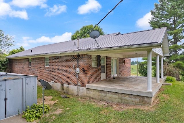 rear view of property featuring metal roof, brick siding, an outdoor structure, a yard, and a shed