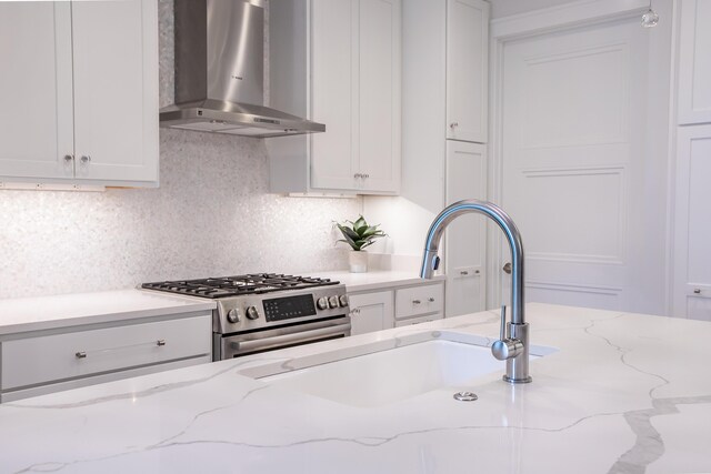 kitchen featuring white cabinetry, high end stove, light stone counters, and wall chimney exhaust hood