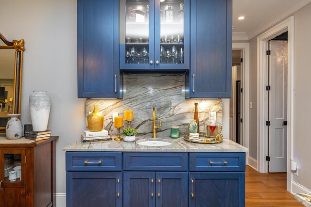 bar with tasteful backsplash, sink, blue cabinetry, wood-type flooring, and ornamental molding