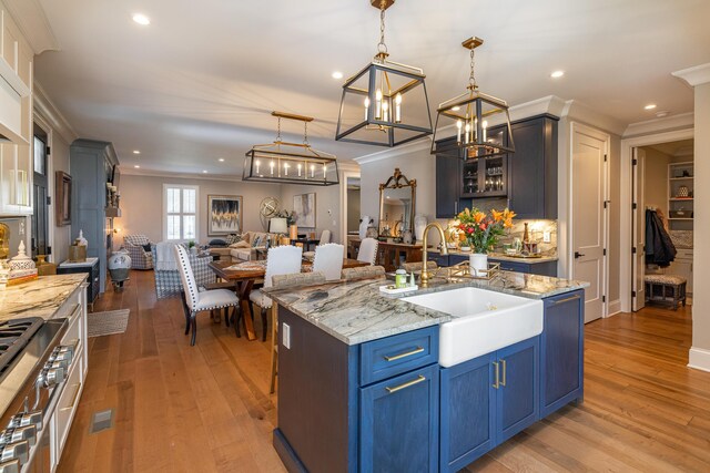 kitchen with crown molding, light wood-type flooring, light stone countertops, decorative light fixtures, and sink