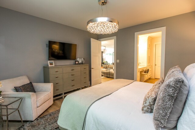 bedroom featuring hardwood / wood-style floors, ensuite bath, and an inviting chandelier