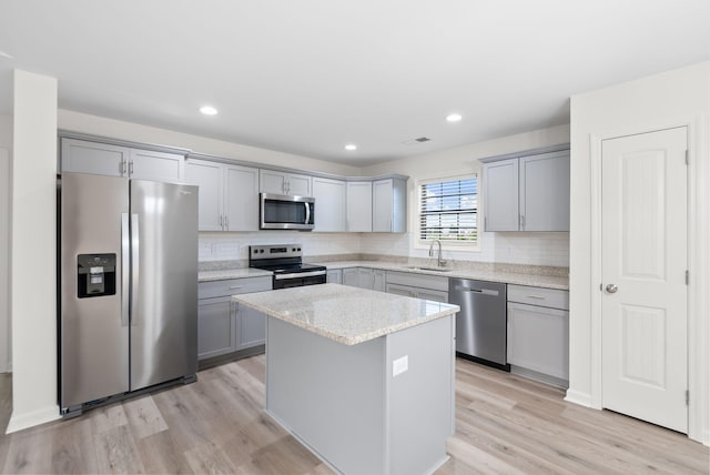 kitchen featuring light wood-type flooring, appliances with stainless steel finishes, tasteful backsplash, and gray cabinetry