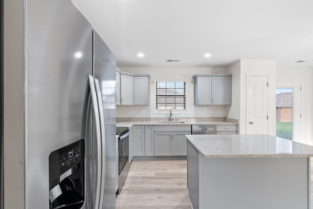 kitchen with light hardwood / wood-style flooring, backsplash, light stone counters, sink, and stainless steel appliances