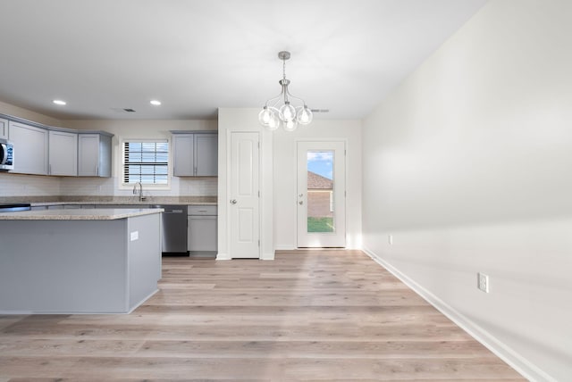 kitchen featuring decorative light fixtures, dishwashing machine, light hardwood / wood-style flooring, light stone counters, and gray cabinetry