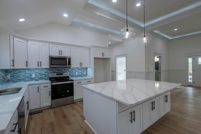 kitchen with hanging light fixtures, a center island, white cabinetry, appliances with stainless steel finishes, and light hardwood / wood-style floors