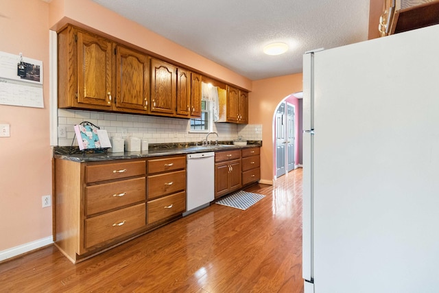 kitchen with a textured ceiling, tasteful backsplash, light wood-type flooring, and white appliances