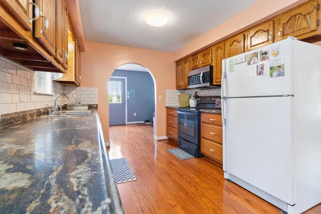 kitchen featuring black electric range oven, white fridge, backsplash, and light wood-type flooring