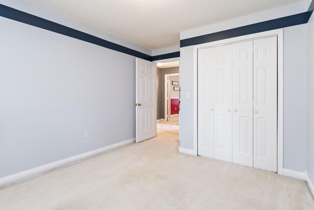 unfurnished bedroom featuring light carpet, a closet, and a textured ceiling