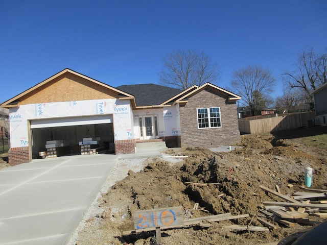 property in mid-construction with a garage, fence, concrete driveway, stone siding, and stucco siding