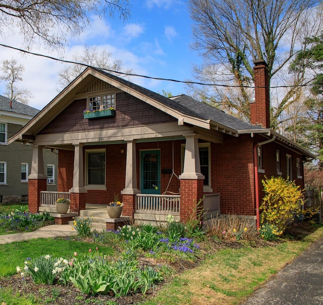 view of front of house featuring a chimney, a porch, and brick siding