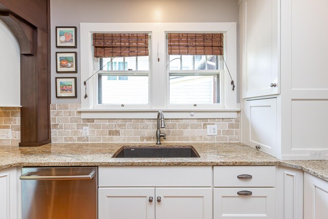 kitchen featuring stainless steel dishwasher, white cabinets, decorative backsplash, sink, and light stone countertops