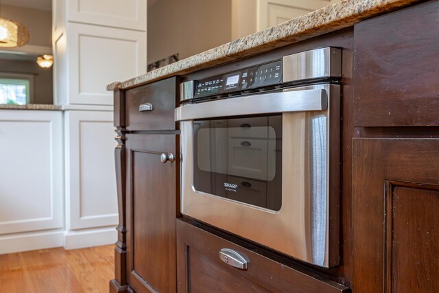 interior details with stainless steel oven, light hardwood / wood-style flooring, white cabinets, and light stone countertops