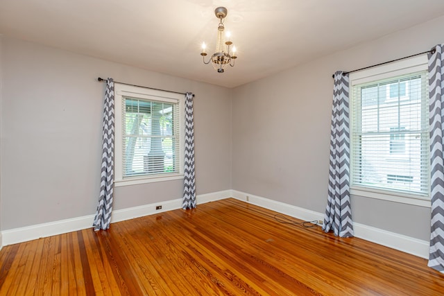 spare room with an inviting chandelier, baseboards, and wood finished floors