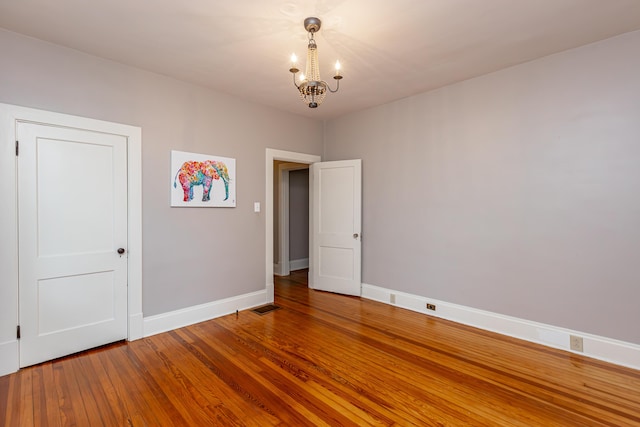 unfurnished room featuring baseboards, a chandelier, wood finished floors, and visible vents