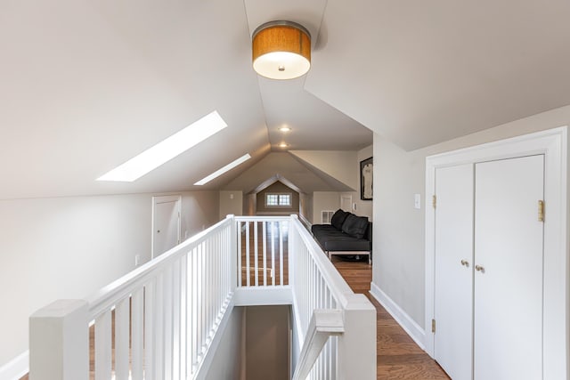 hall featuring baseboards, an upstairs landing, wood finished floors, and vaulted ceiling with skylight