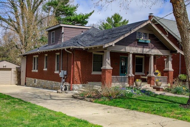 view of front facade featuring brick siding, an outbuilding, driveway, and covered porch