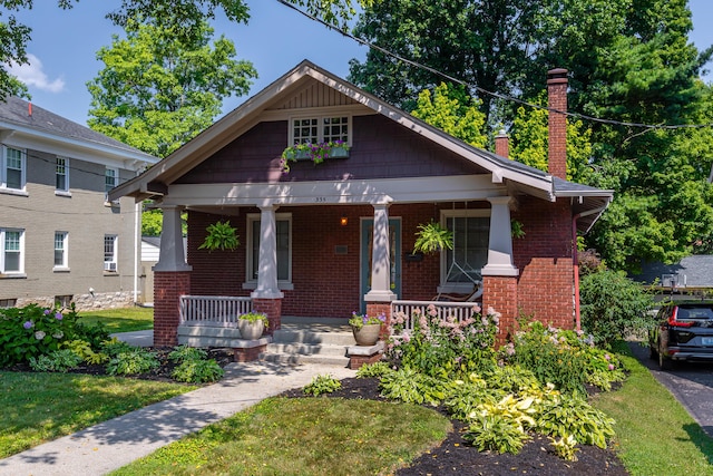 view of front facade featuring a porch, brick siding, a chimney, and a front yard
