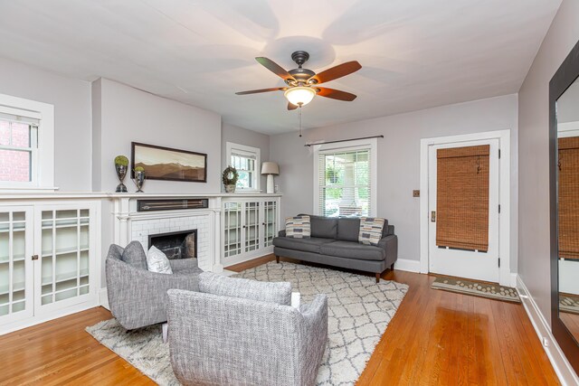 living room featuring a fireplace, ceiling fan, and light wood-type flooring