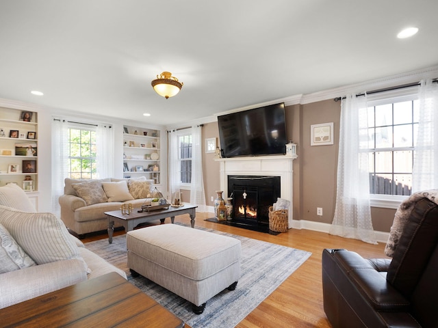 living room with built in shelves, crown molding, and light hardwood / wood-style flooring