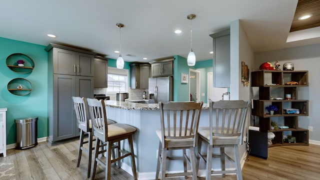 kitchen with stainless steel refrigerator with ice dispenser, hanging light fixtures, gray cabinetry, light stone countertops, and decorative backsplash