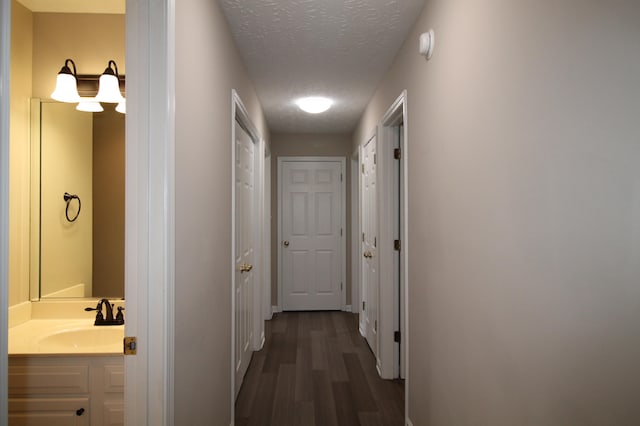 corridor featuring sink, a textured ceiling, and dark hardwood / wood-style flooring