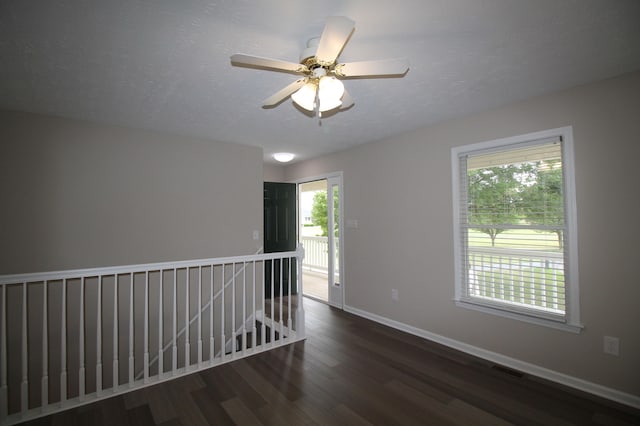 empty room with a textured ceiling, a wealth of natural light, ceiling fan, and dark hardwood / wood-style floors