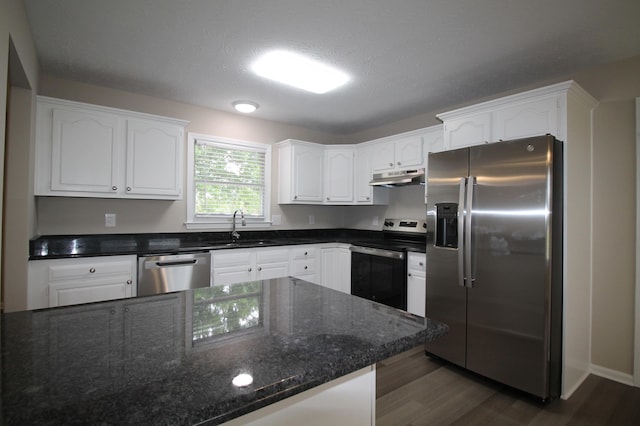 kitchen featuring stainless steel appliances, sink, dark hardwood / wood-style floors, dark stone countertops, and white cabinetry