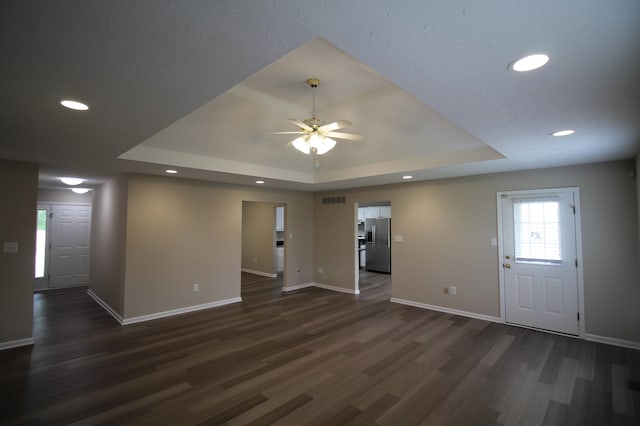 unfurnished living room with dark hardwood / wood-style floors, ceiling fan, and a raised ceiling