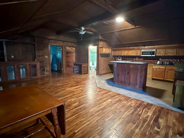 kitchen featuring ceiling fan, hardwood / wood-style floors, lofted ceiling with beams, and tasteful backsplash