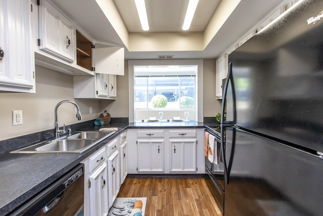 kitchen with dark wood-type flooring, sink, black appliances, a tray ceiling, and white cabinets