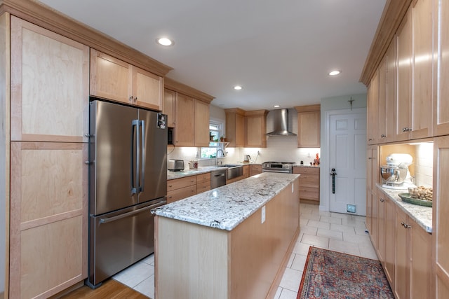 kitchen with light brown cabinets, backsplash, light stone counters, stainless steel appliances, and wall chimney exhaust hood