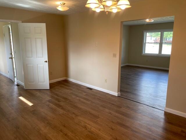 spare room featuring an inviting chandelier and dark hardwood / wood-style floors