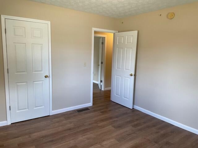 unfurnished bedroom with a textured ceiling and dark hardwood / wood-style flooring