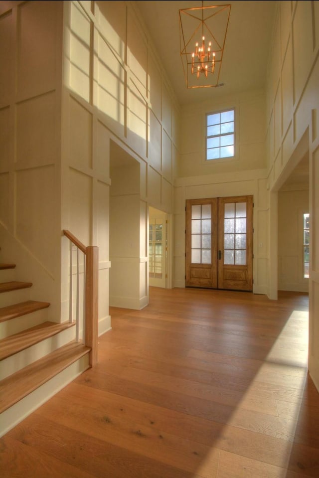 interior space with an inviting chandelier, light wood-type flooring, french doors, and a high ceiling