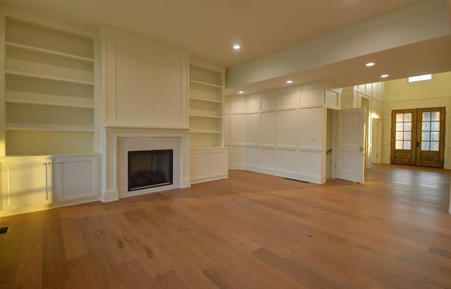 unfurnished living room featuring french doors, light wood-type flooring, a high end fireplace, and built in shelves