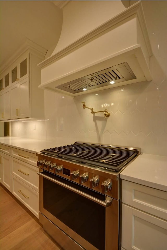 kitchen with light hardwood / wood-style floors, white cabinets, decorative backsplash, stainless steel range with gas cooktop, and wall chimney exhaust hood