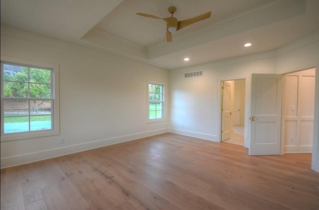 spare room with ceiling fan, a raised ceiling, and light wood-type flooring