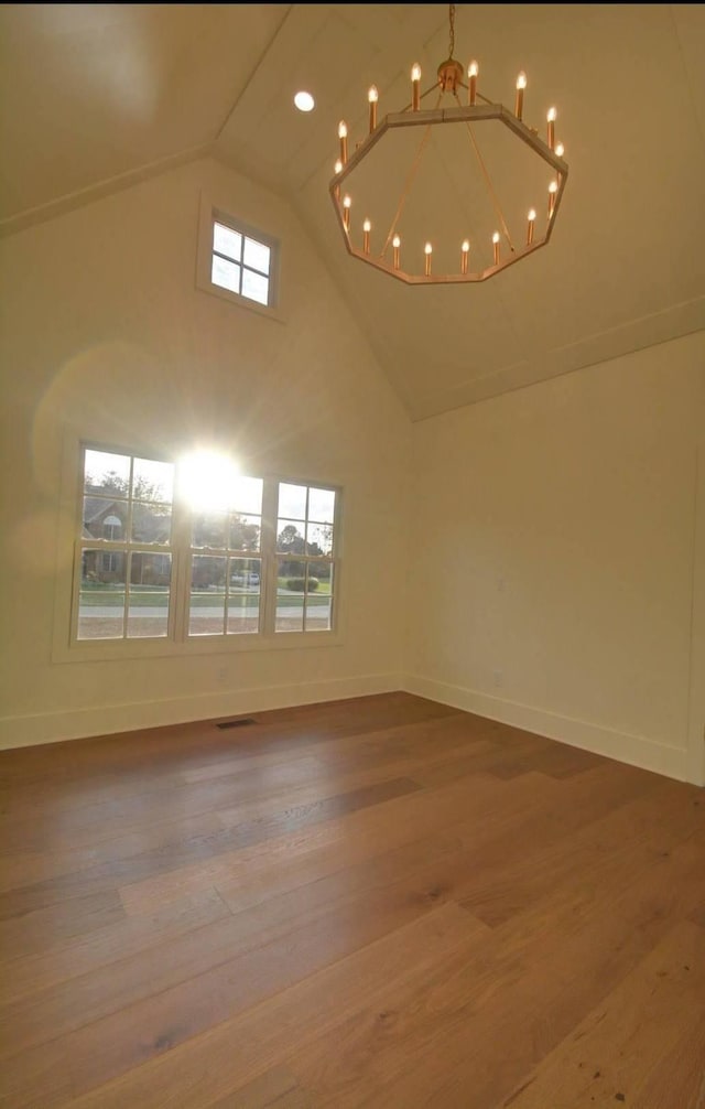 unfurnished room with vaulted ceiling, hardwood / wood-style floors, and an inviting chandelier