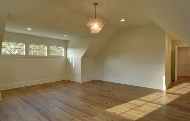 additional living space featuring lofted ceiling, a chandelier, and light wood-type flooring