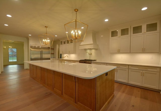 kitchen featuring pendant lighting, white cabinetry, stainless steel appliances, custom range hood, and a large island with sink