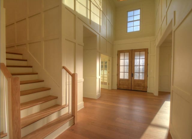 entrance foyer with a towering ceiling, french doors, and light wood-type flooring