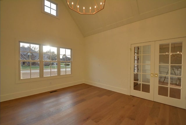 empty room featuring wood-type flooring, a chandelier, high vaulted ceiling, and french doors